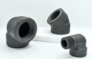 Three black threaded A105 metal pipe fittings of varying angles and sizes are positioned on a white surface with a light background. One fitting is propped on a white block for emphasis, highlighting quality and recent pricing update.